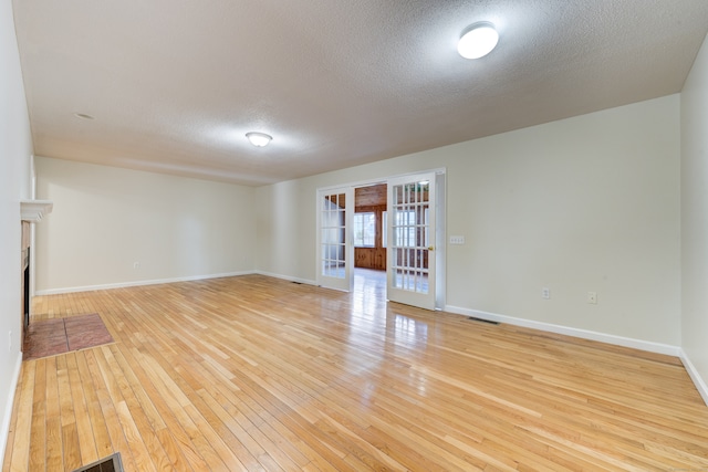 empty room featuring light wood-type flooring, french doors, and a textured ceiling