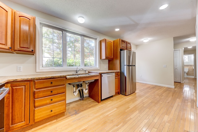 kitchen with light hardwood / wood-style floors, sink, light stone counters, appliances with stainless steel finishes, and a textured ceiling