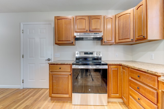 kitchen featuring light stone counters, light wood-type flooring, and stainless steel electric range