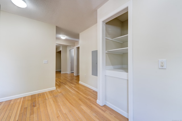 hallway featuring electric panel, light wood-type flooring, and a textured ceiling