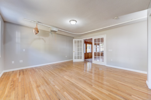 spare room with a textured ceiling, french doors, and light hardwood / wood-style flooring