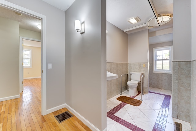 bathroom with wood-type flooring, tile walls, a textured ceiling, and toilet