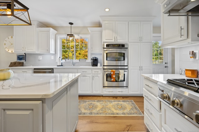 kitchen with hanging light fixtures, sink, white cabinetry, stainless steel appliances, and light hardwood / wood-style floors