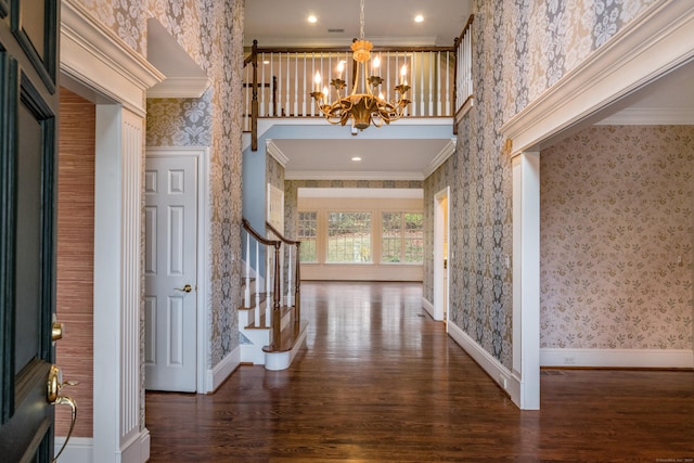 entryway featuring an inviting chandelier, a towering ceiling, dark hardwood / wood-style flooring, and ornamental molding