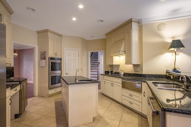 kitchen featuring premium range hood, stainless steel appliances, sink, and an island with sink