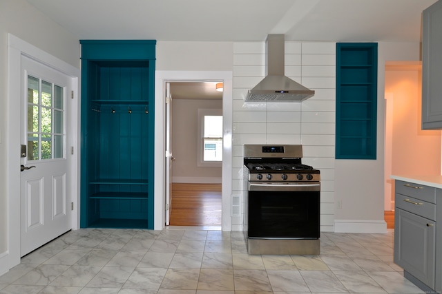 kitchen with stainless steel range with gas cooktop, wall chimney range hood, light hardwood / wood-style floors, and gray cabinetry