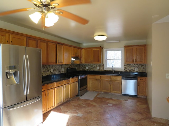 kitchen with dark countertops, a sink, stainless steel appliances, under cabinet range hood, and backsplash