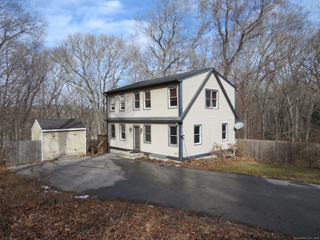 view of front of property featuring aphalt driveway, fence, an outdoor structure, and a shed