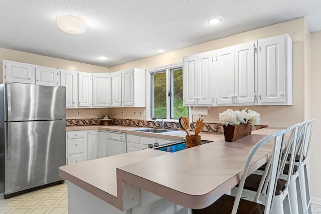 kitchen featuring stainless steel fridge, kitchen peninsula, white cabinetry, and a kitchen bar