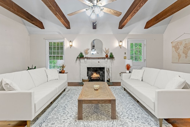 living room with a brick fireplace, light hardwood / wood-style floors, beamed ceiling, and ceiling fan