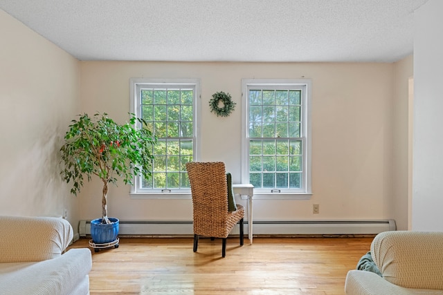 sitting room featuring a textured ceiling, light wood-type flooring, and a baseboard heating unit