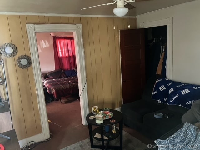 living room featuring ceiling fan, wooden walls, ornamental molding, and carpet