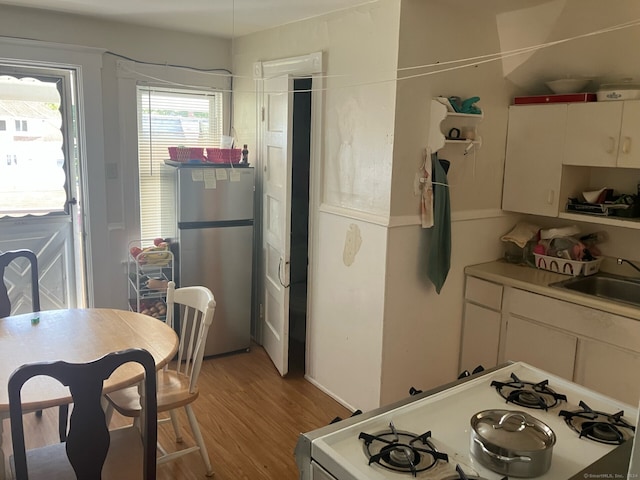 kitchen featuring white cabinets, sink, white gas range, stainless steel refrigerator, and light hardwood / wood-style floors