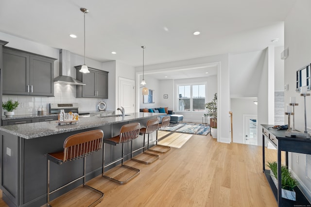 kitchen featuring pendant lighting, wall chimney range hood, a kitchen breakfast bar, dark stone countertops, and light hardwood / wood-style floors