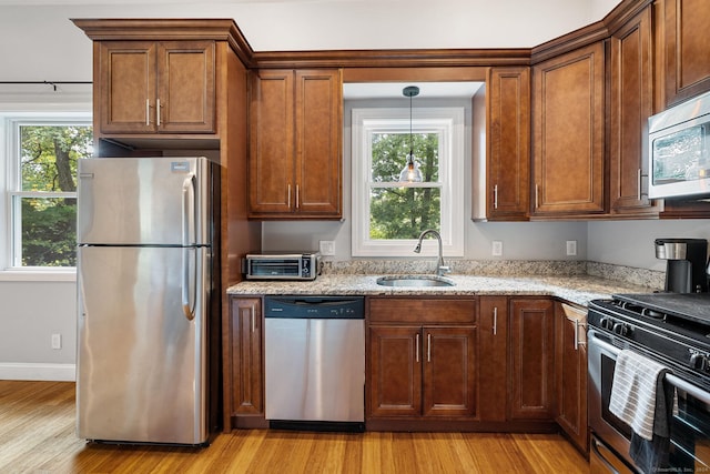 kitchen with baseboards, appliances with stainless steel finishes, light stone counters, light wood-type flooring, and a sink