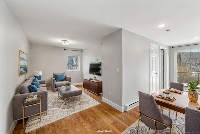 living room featuring light wood finished floors, baseboards, baseboard heating, and a wealth of natural light