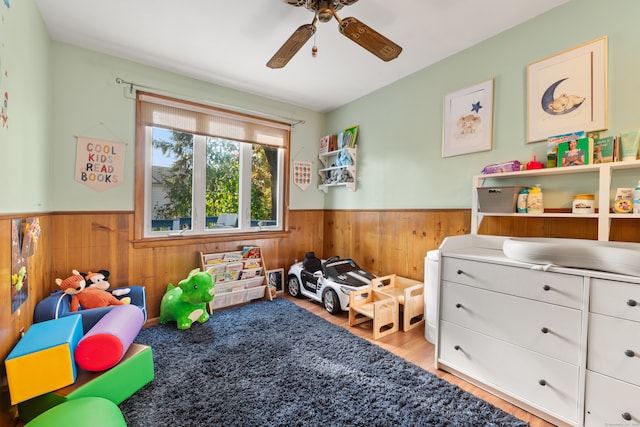 recreation room with wooden walls, light wood-type flooring, and ceiling fan