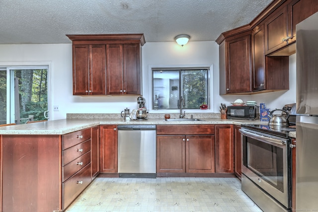 kitchen featuring stainless steel appliances, kitchen peninsula, sink, and a textured ceiling