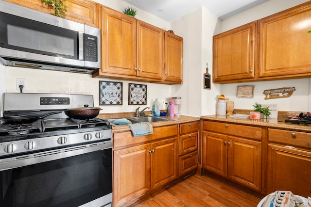 kitchen with appliances with stainless steel finishes, sink, and light hardwood / wood-style floors