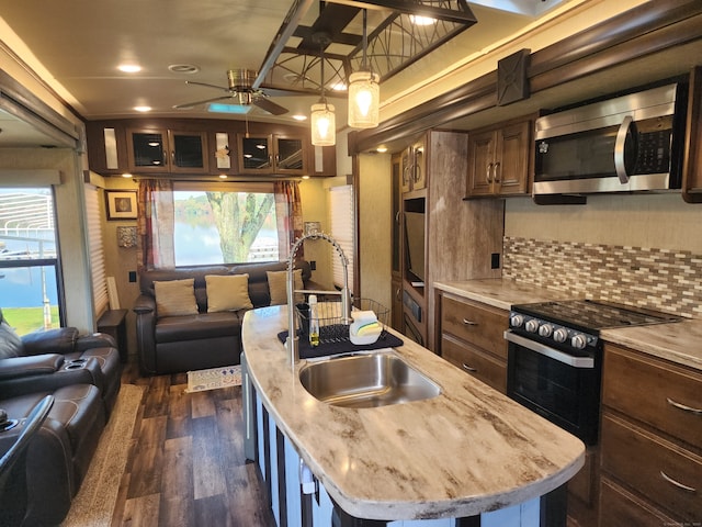 kitchen with sink, a center island with sink, dark wood-type flooring, range, and decorative backsplash