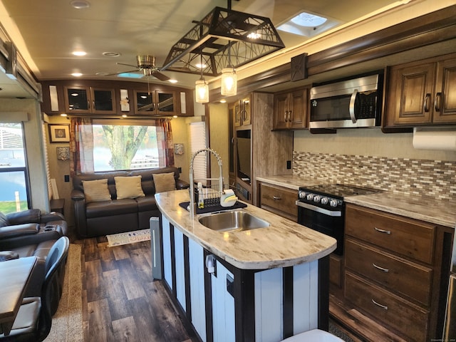 kitchen with dark wood-type flooring, a center island with sink, sink, light stone counters, and appliances with stainless steel finishes