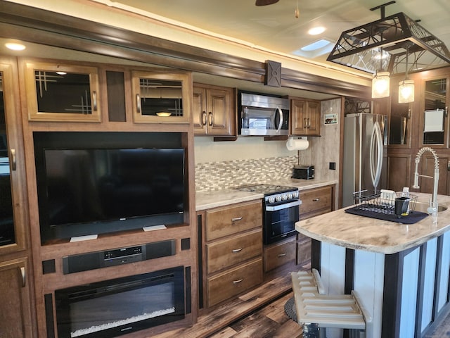 kitchen with brown cabinetry, appliances with stainless steel finishes, decorative light fixtures, backsplash, and dark wood-style flooring