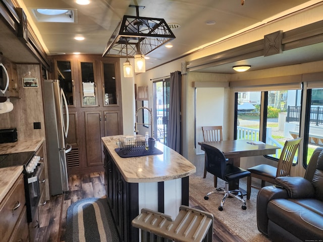 interior space with hanging light fixtures, a sink, appliances with stainless steel finishes, dark wood-style floors, and a kitchen island