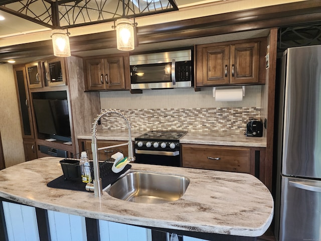 kitchen with pendant lighting, sink, light stone countertops, backsplash, and appliances with stainless steel finishes