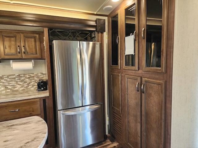 kitchen with tasteful backsplash, light stone countertops, stainless steel refrigerator, and wood-type flooring