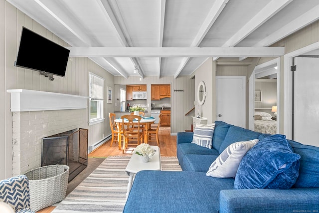 living room featuring wooden walls, beam ceiling, a fireplace, and light hardwood / wood-style flooring