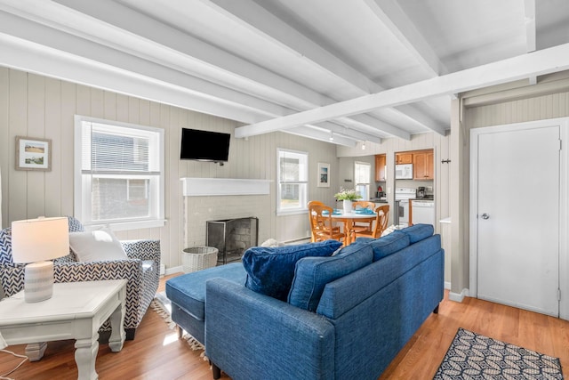 living room featuring wood walls, a brick fireplace, light hardwood / wood-style floors, and beam ceiling