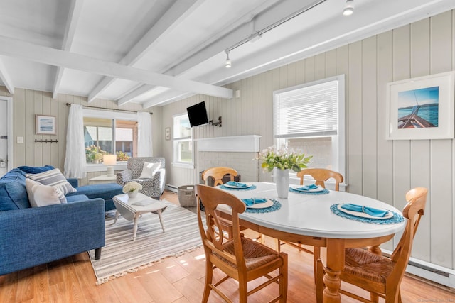 dining room with a fireplace, beam ceiling, wood walls, and light hardwood / wood-style floors