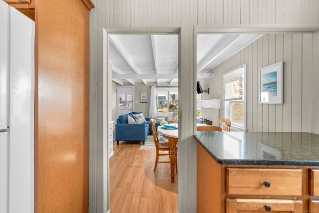 kitchen with wood walls, beamed ceiling, light hardwood / wood-style flooring, dark stone countertops, and white fridge