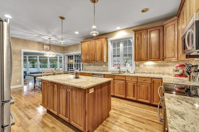 kitchen with light stone countertops, light wood-type flooring, stainless steel appliances, pendant lighting, and a center island