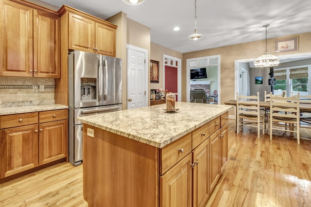 kitchen with stainless steel fridge, pendant lighting, a fireplace, a center island, and light hardwood / wood-style floors