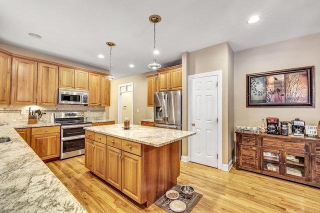 kitchen featuring hanging light fixtures, appliances with stainless steel finishes, tasteful backsplash, light hardwood / wood-style floors, and light stone counters