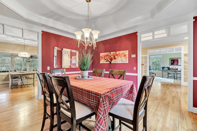 dining space featuring a raised ceiling, ornamental molding, a notable chandelier, and light wood-type flooring