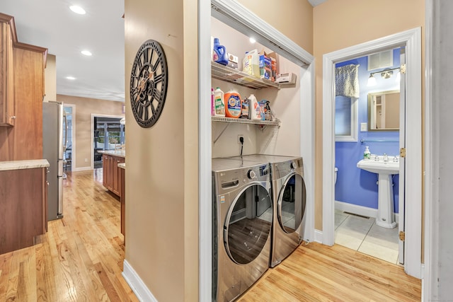 laundry area with washer and clothes dryer, light wood-type flooring, and sink