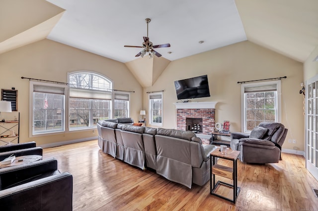 living room with a wealth of natural light, a fireplace, ceiling fan, and light wood-type flooring