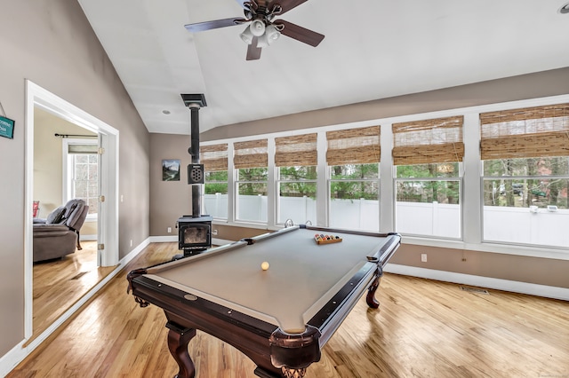 playroom with a wood stove, plenty of natural light, vaulted ceiling, and light hardwood / wood-style flooring