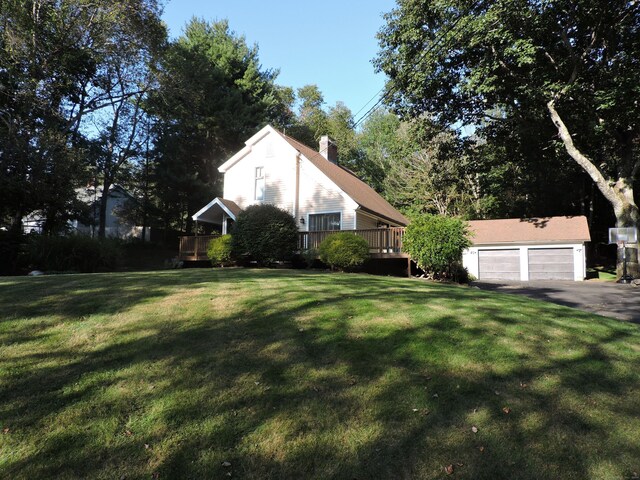 exterior space featuring a garage, a deck, a lawn, and an outbuilding