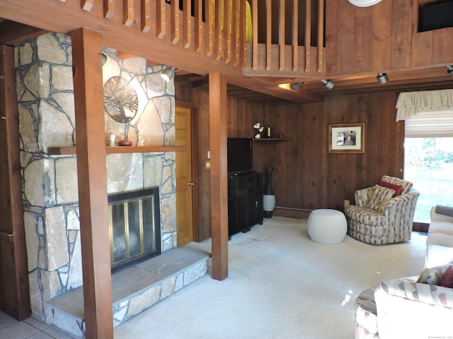 carpeted living room with wood walls and a stone fireplace