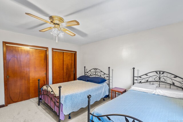 bedroom with ceiling fan, multiple closets, and light colored carpet