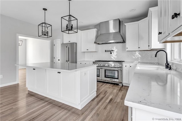 kitchen with premium appliances, wall chimney range hood, a center island, and white cabinets