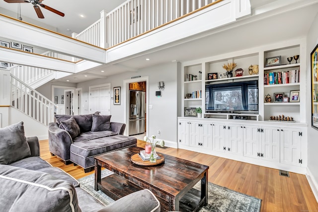 living room with light wood-type flooring, a towering ceiling, ceiling fan, and built in features