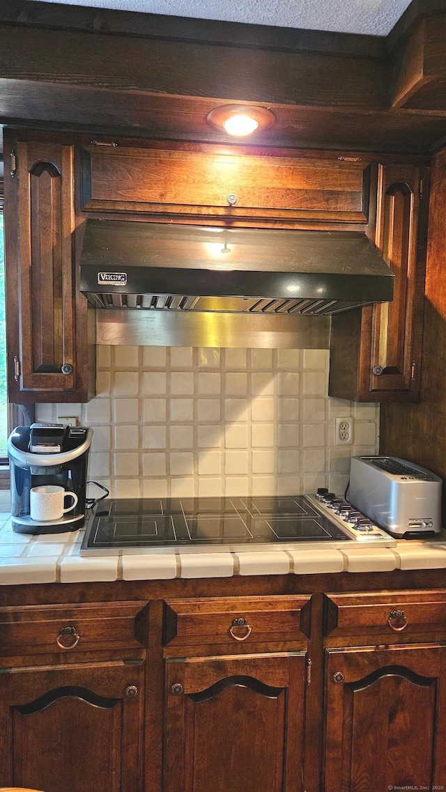 kitchen with gas stovetop, dark brown cabinetry, custom range hood, and tasteful backsplash