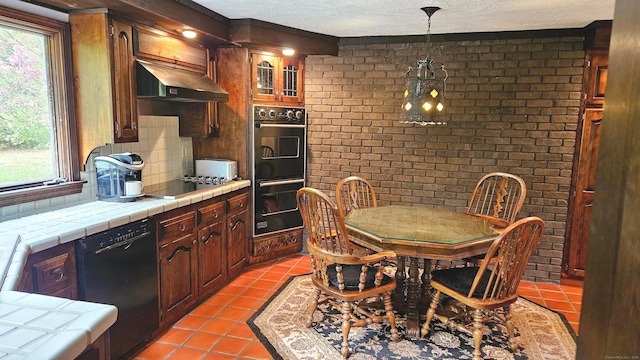 kitchen with black appliances, tile counters, brick wall, and a wealth of natural light