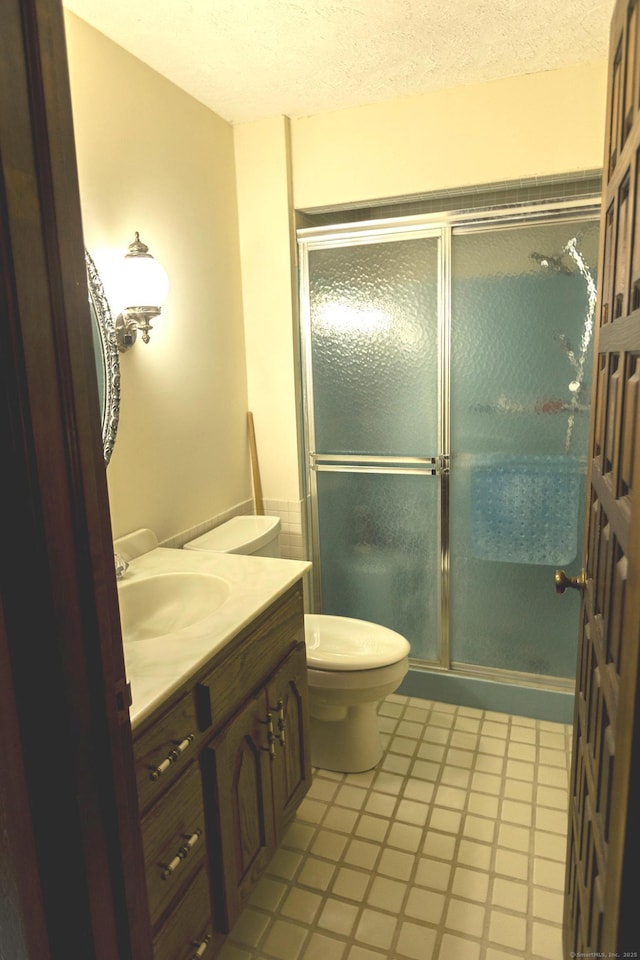 bathroom with a textured ceiling, vanity, an enclosed shower, and toilet