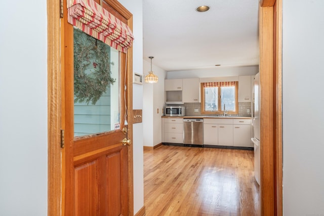 kitchen with hanging light fixtures, stainless steel appliances, tasteful backsplash, light hardwood / wood-style flooring, and white cabinets