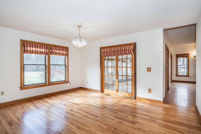 empty room with light hardwood / wood-style floors, a healthy amount of sunlight, and a notable chandelier